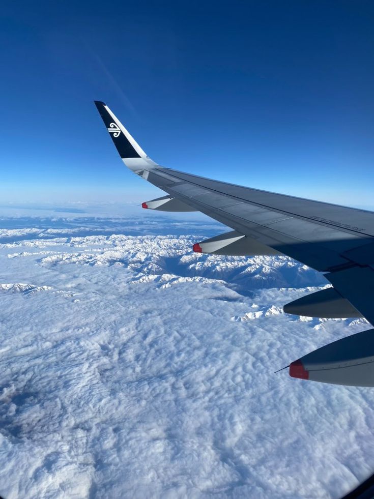 the wing of an airplane flying over snow covered ground