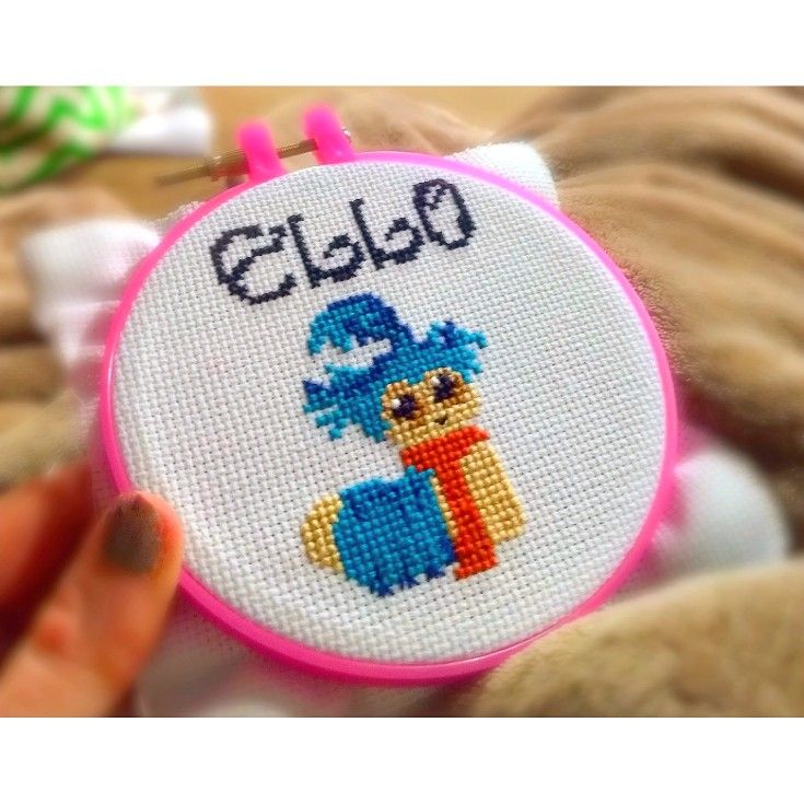 someone is holding up a cross - stitch project in front of a teddy bear's face