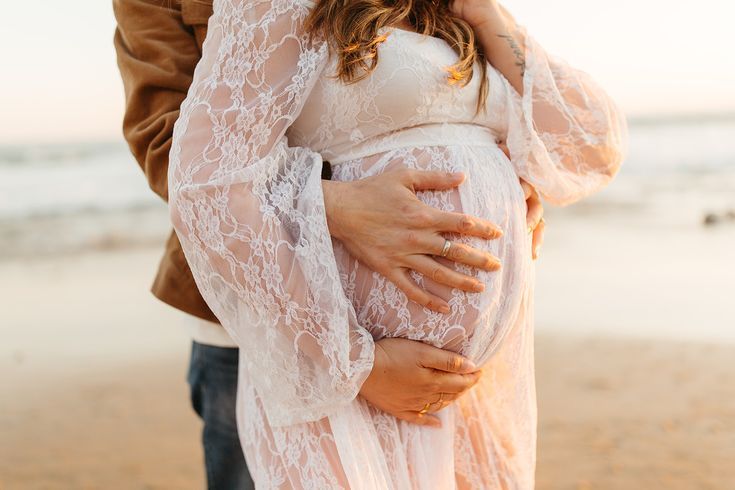 a pregnant woman holding her husband's belly on the beach