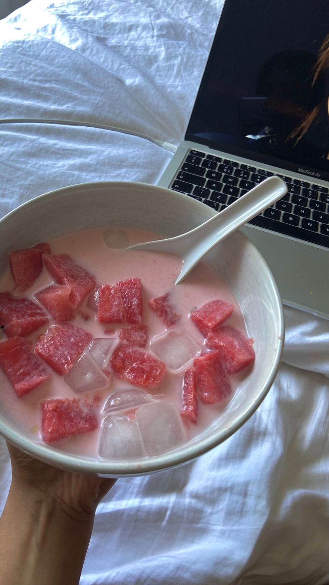 a person holding a bowl of watermelon and ice in front of a laptop