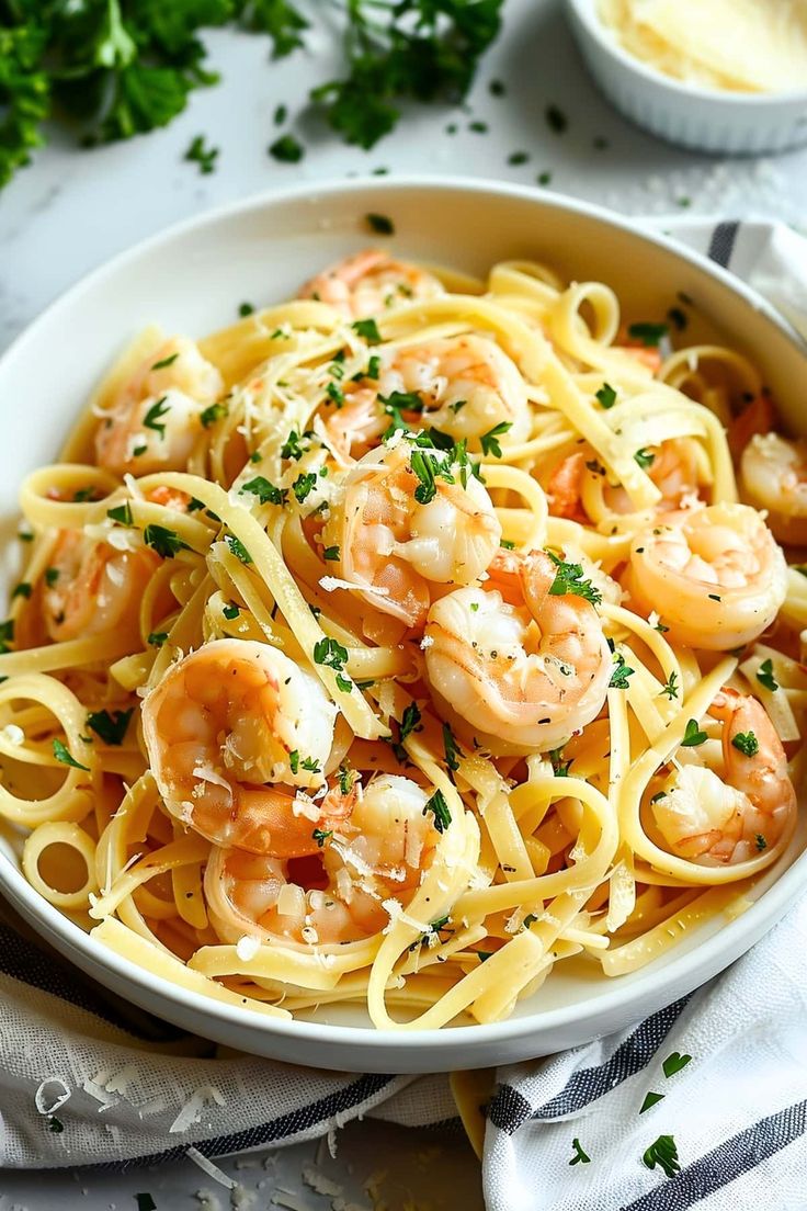 a white bowl filled with pasta and shrimp on top of a table next to parsley