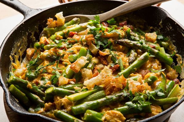 asparagus and eggs in a skillet with a wooden spoon on the side