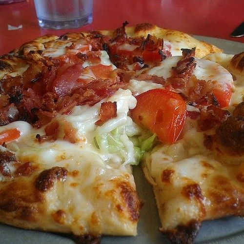 a pizza with bacon, tomatoes and lettuce on it sitting on a plate