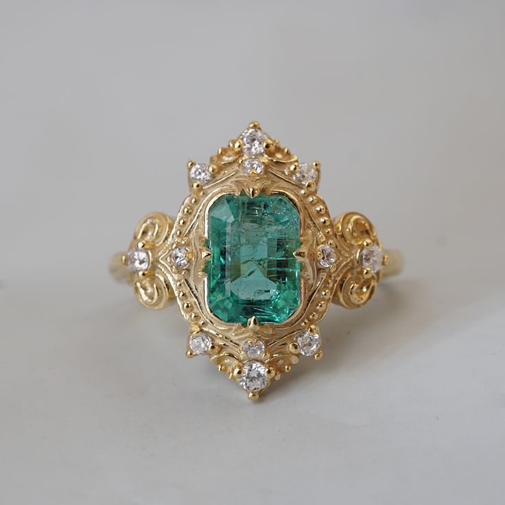 an emerald and diamond ring on a white surface with gold filigrees around it