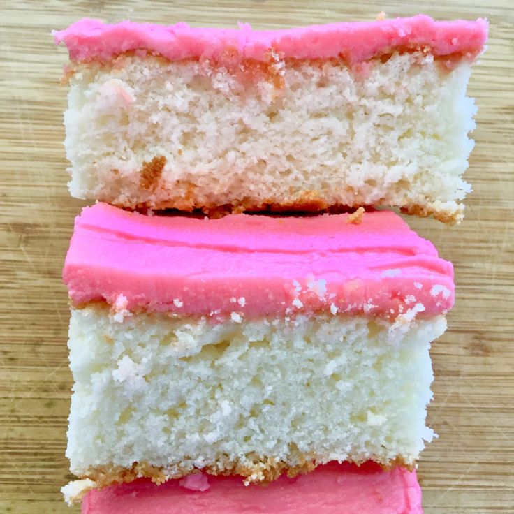 three pieces of white and pink cake on a wooden table with one slice cut out