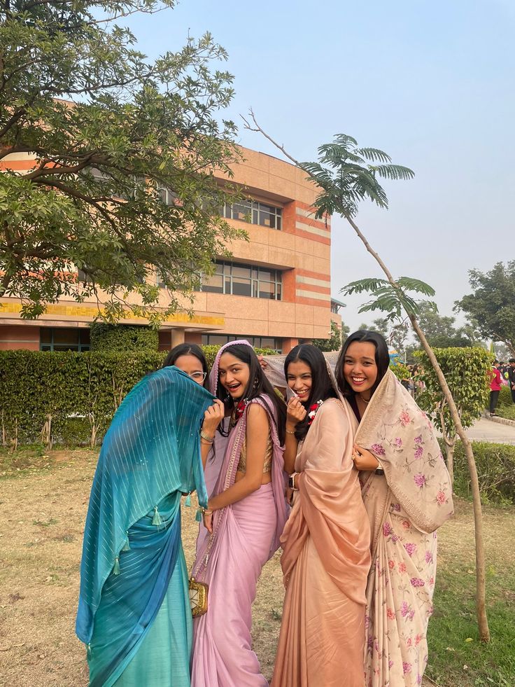 four women in sari posing for the camera outside an office building with trees and bushes behind them