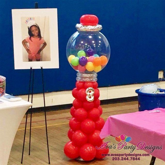 there is a gumball machine with balloons in it on the floor next to a table