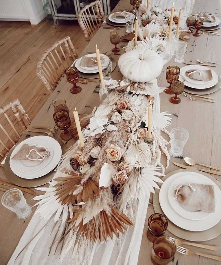 the table is set with white plates and silverware, gold candlesticks and feathers