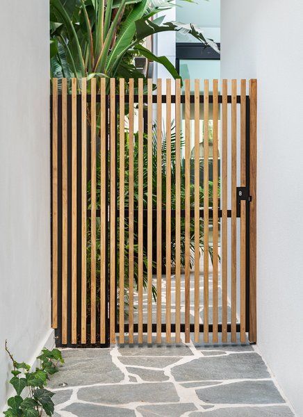 an open wooden gate on the side of a building next to a stone walkway and potted plant