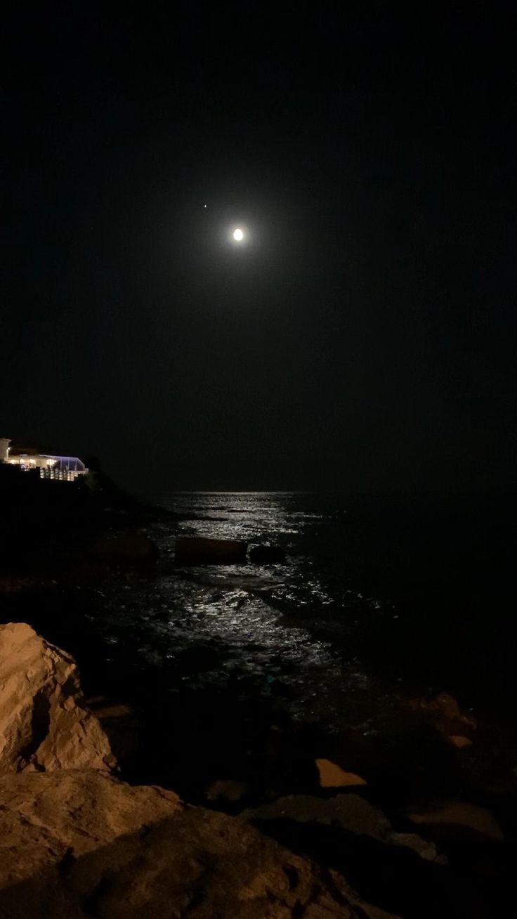 the moon is shining over the ocean at night