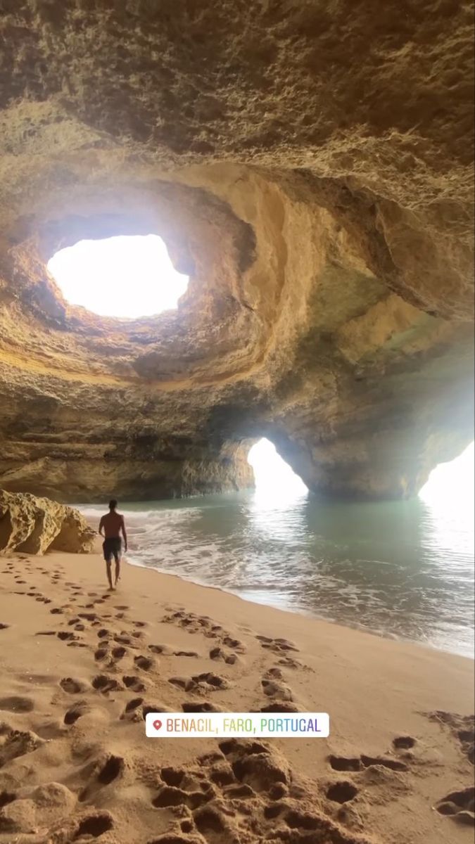 a man walking on the beach in front of a cave