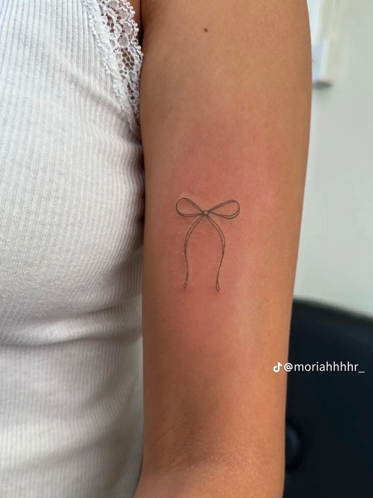 a woman's arm with a small bow tattoo on the back of her arm