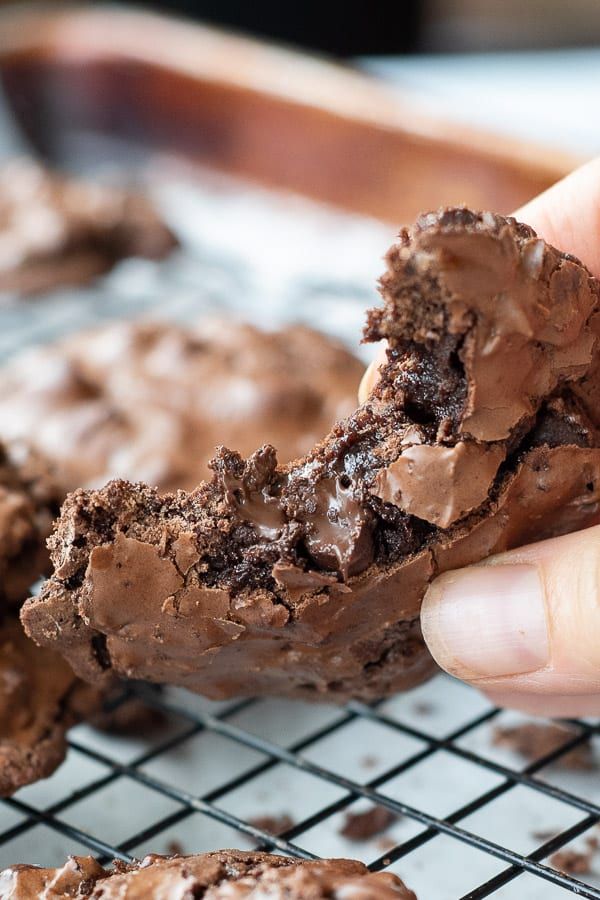 a person holding a chocolate cookie in front of some cookies on a cooling wire rack