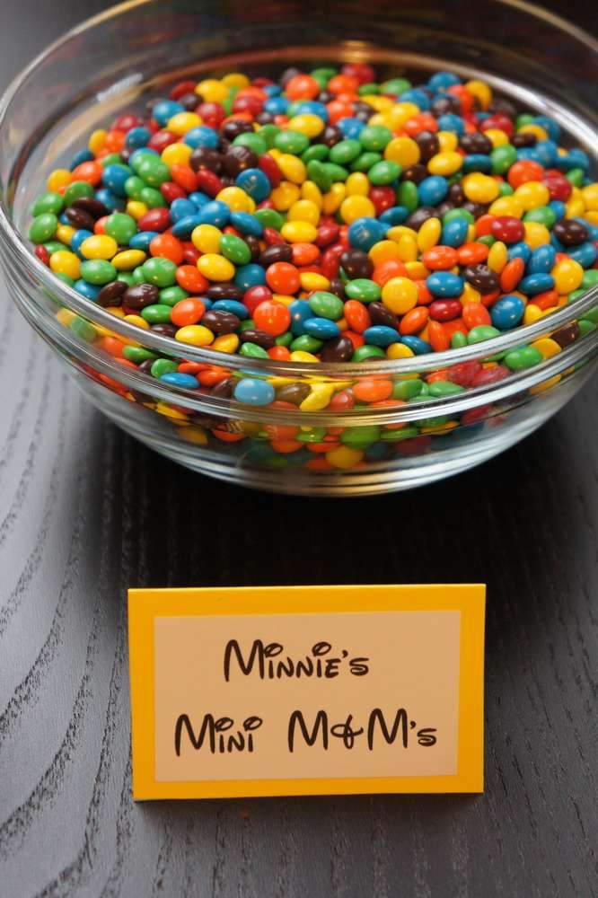 a bowl filled with lots of colorful candy next to a sign that says minnie's mini m & m