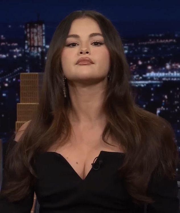 a woman with long hair sitting down in front of a tv screen and looking off to the side