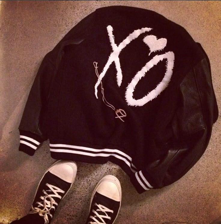 a black jacket with white letters on it and two pairs of shoes next to it