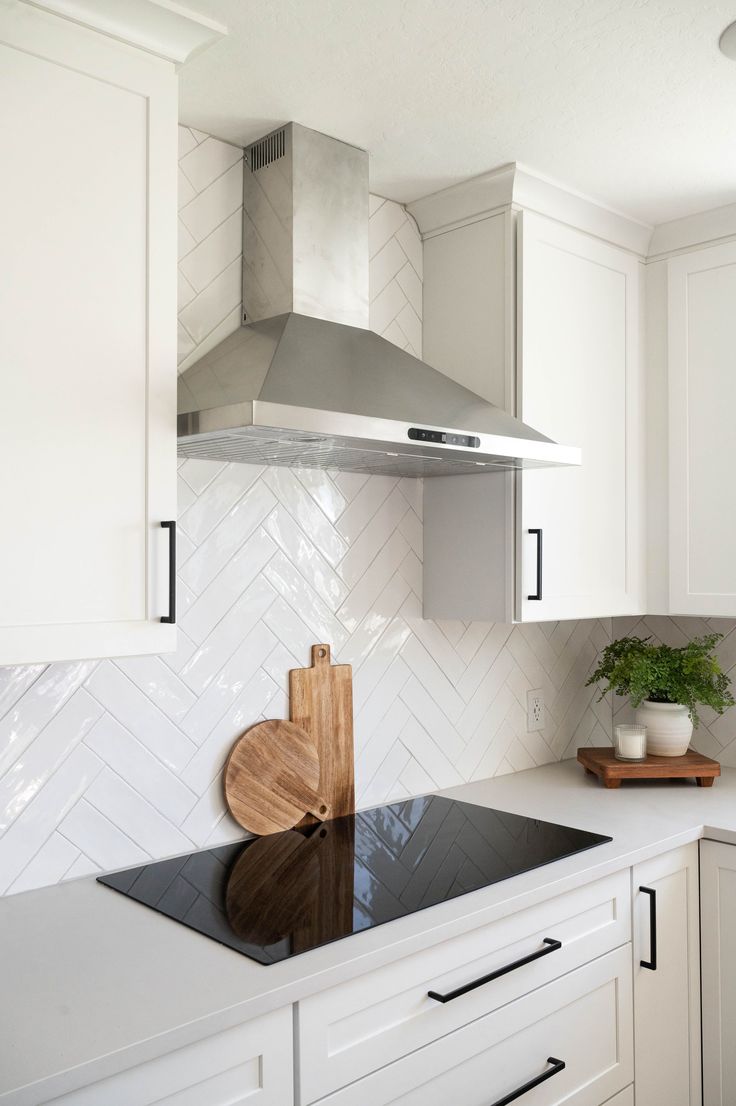 a kitchen with white cabinets and black counter tops, an oven hood and cutting board