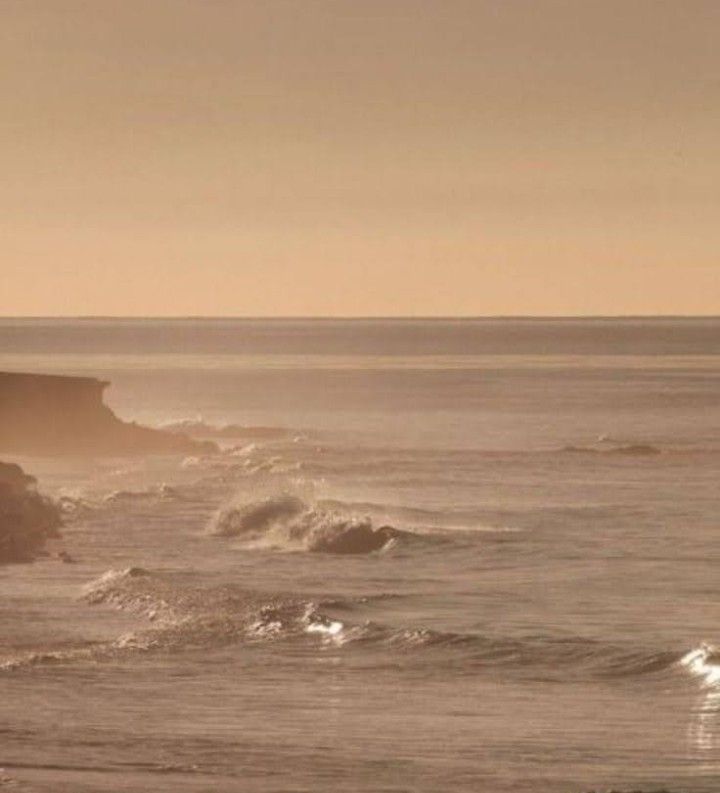 two surfers are riding the waves on their surfboards in front of an ocean cliff