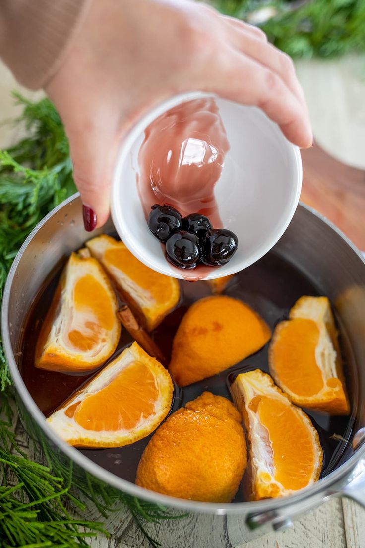 someone is adding olives to orange slices in a pot