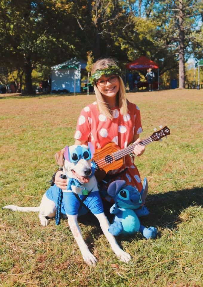 a woman sitting in the grass with her dog and ukulele on her lap