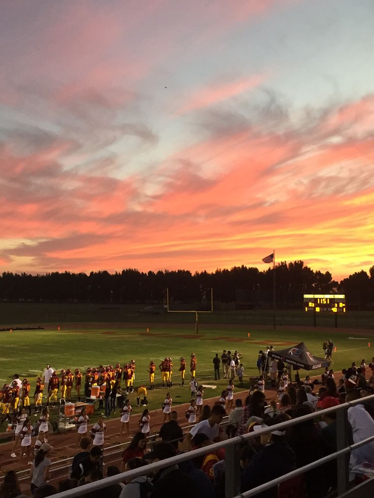 a group of people standing on top of a field next to a soccer field at sunset