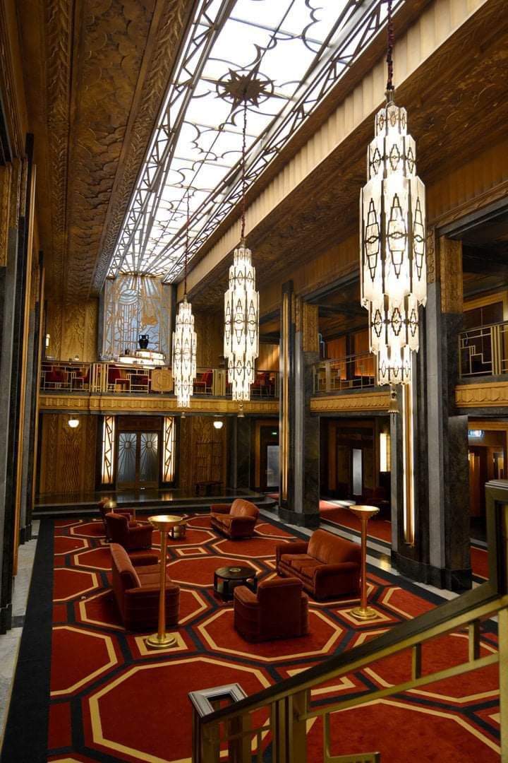 an ornate lobby with chandeliers and chairs in the foreground, lights hanging from the ceiling