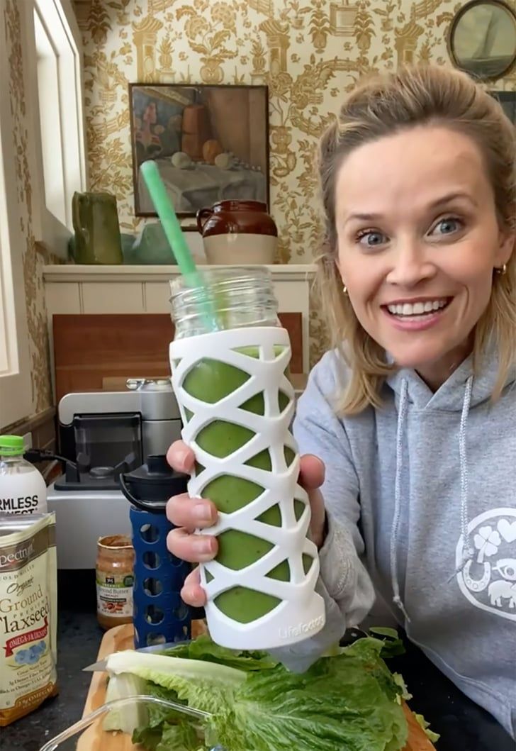 a woman holding up a cup with a straw in it and vegetables on the table