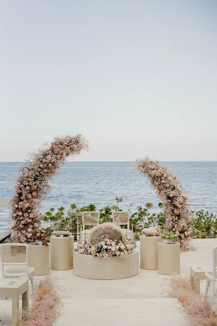 an outdoor wedding setup with flowers on the arch and water in the backround