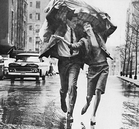 black and white photograph of two men running in the rain with umbrellas over their heads