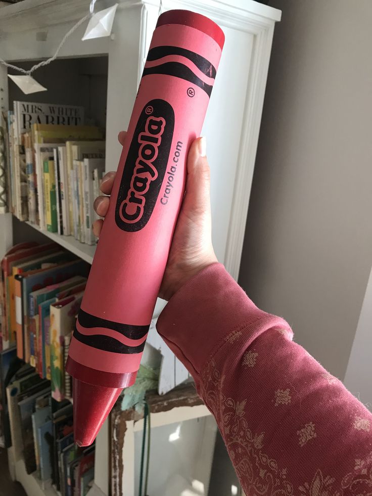 a person holding up a pink candy tube in front of a bookshelf