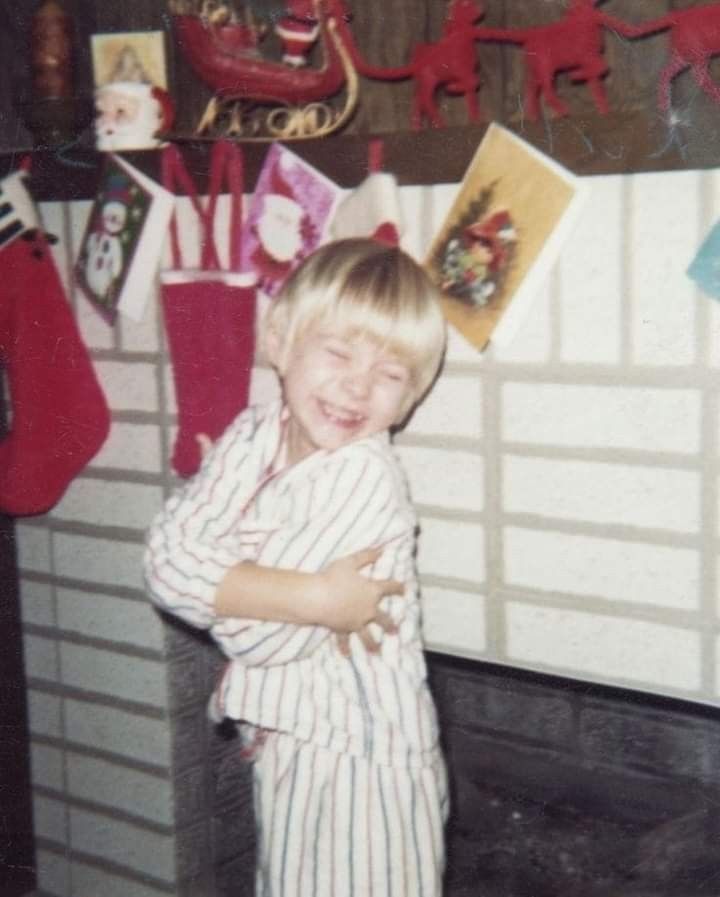 a young boy standing in front of a fireplace with stockings on the wall behind him