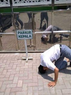 a man bending over on the ground in front of a parking sign that reads parkir kepala