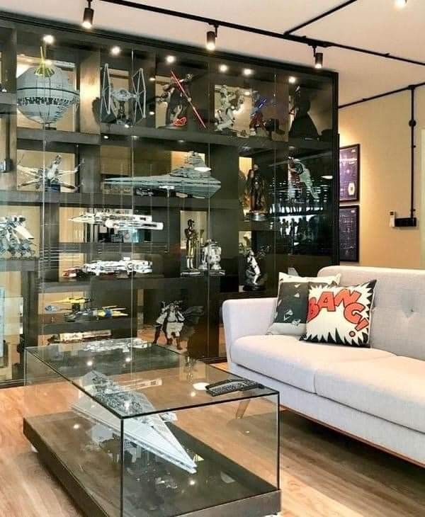 a living room filled with furniture and shelves full of action figures in glass cases on top of hard wood flooring