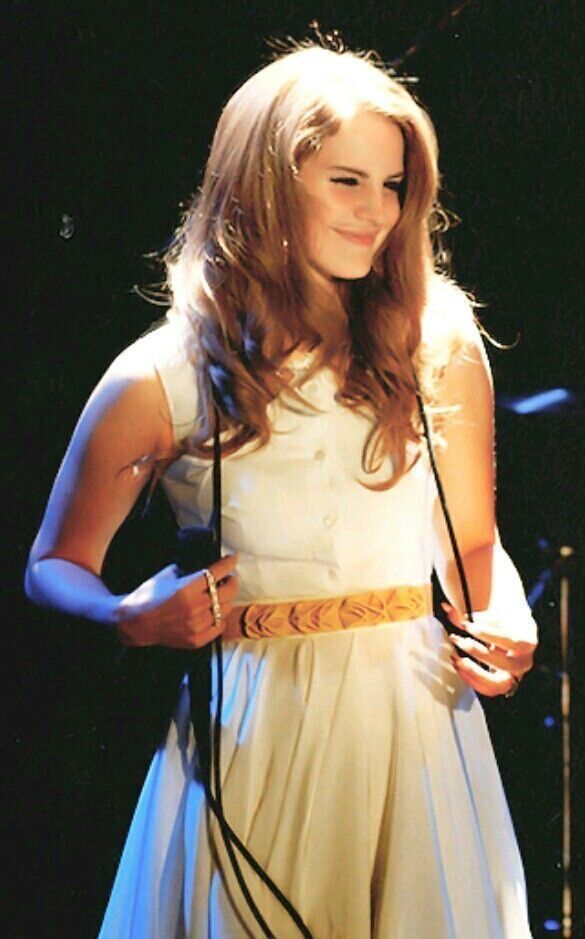 a woman in a white dress holding a microphone and standing next to a drum set