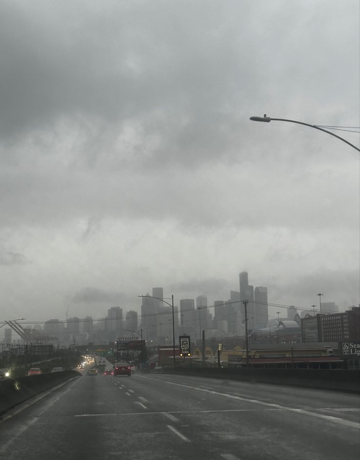 cars driving down an empty highway in front of a large city on a cloudy day