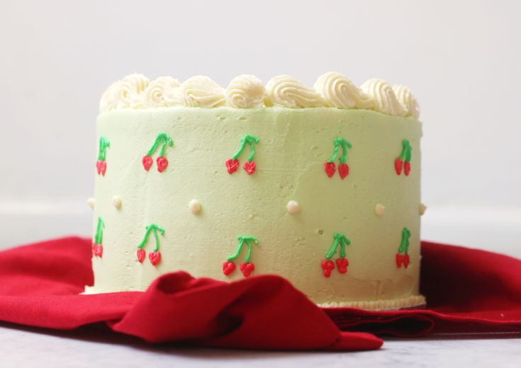 a cake with white frosting and cherries on it sitting on a red cloth