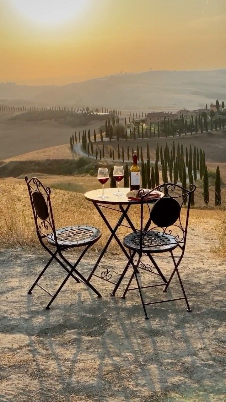 two chairs and a table with wine on it in the middle of an open field