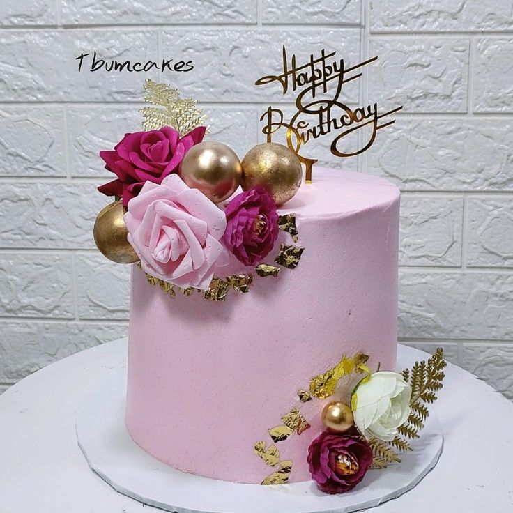 a pink and gold birthday cake with flowers on top