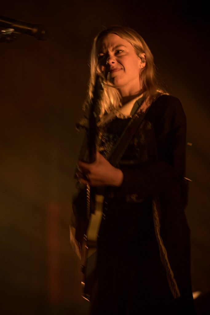 a woman standing in front of a microphone and holding an acoustic guitar while singing into a microphone