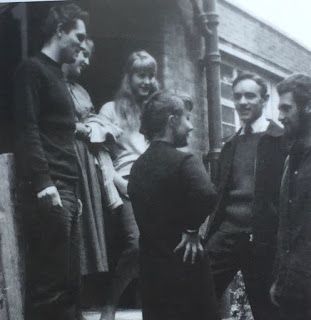 a group of people standing around each other in front of a building with the door open