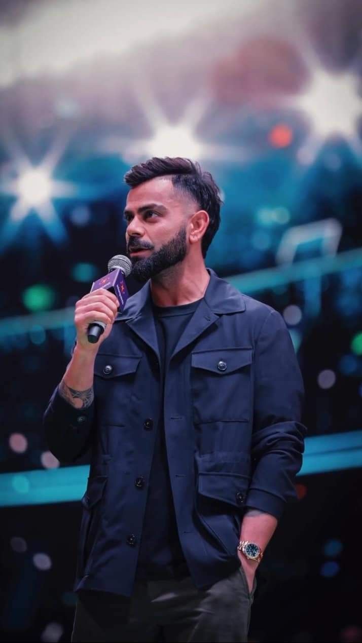 a man holding a microphone in his right hand while standing next to a stage with lights behind him