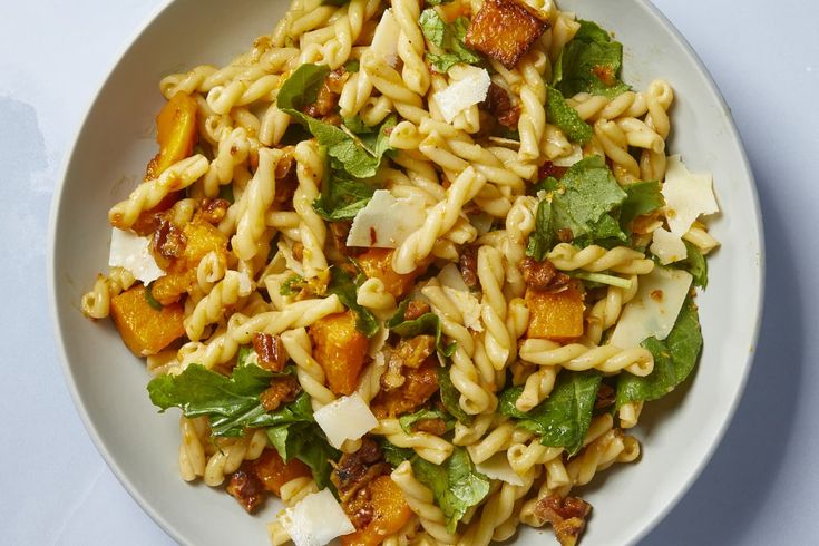 a white bowl filled with pasta and greens on top of a blue table cloth next to a fork