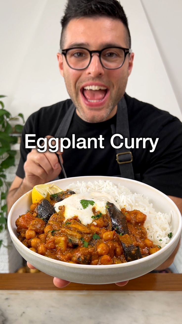 a man holding a bowl of food with rice and eggplant curry