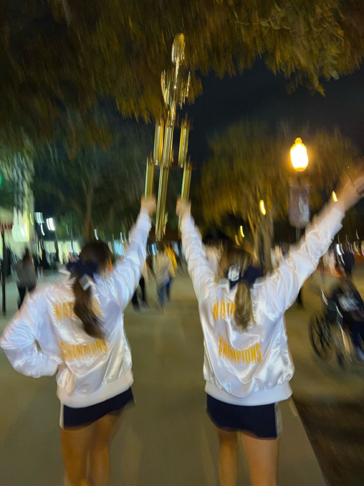 two cheerleaders holding up their trophies in the air