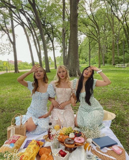 three women sitting at a picnic table with food and drinks in front of their faces