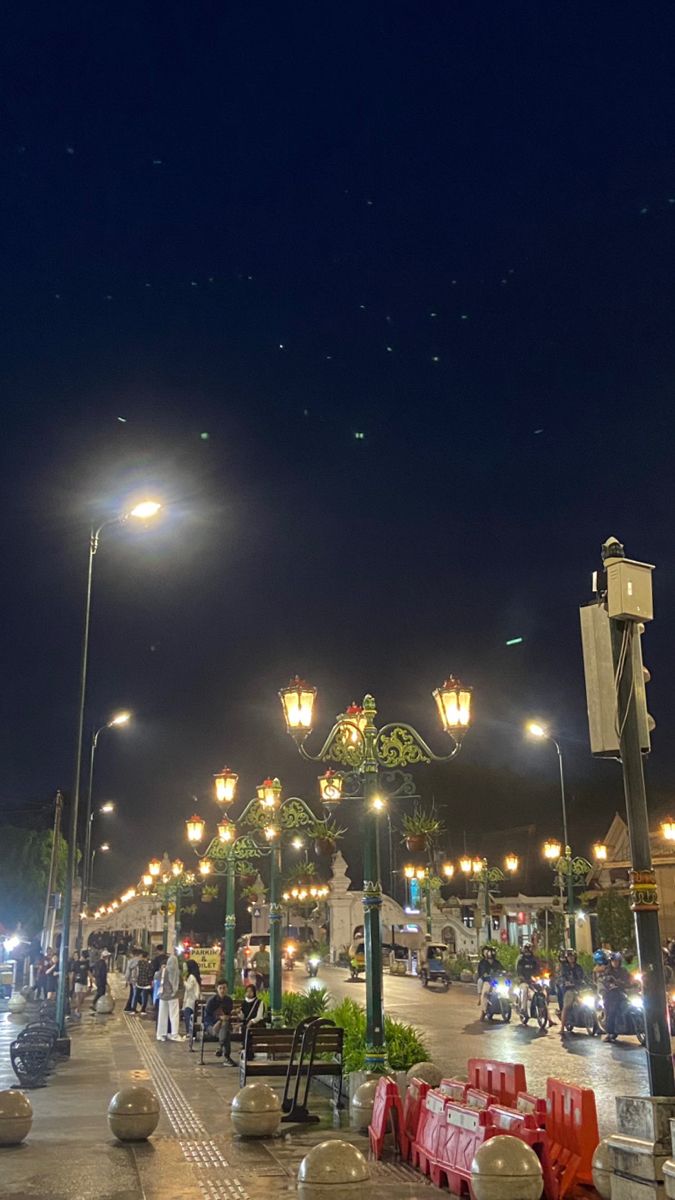 people are walking down the street at night with lights and lanterns on either side of them