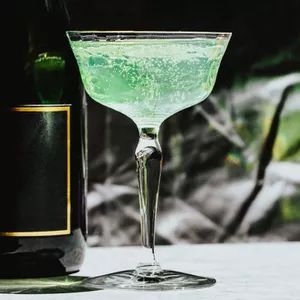 a green drink in a glass next to a bottle