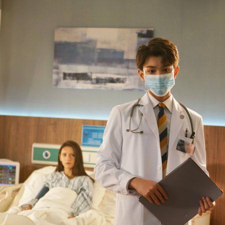 a man in a white lab coat and tie holding a clipboard while standing next to a woman in a hospital bed