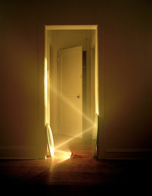 an open door with the light shining through it and a broom laying on the floor