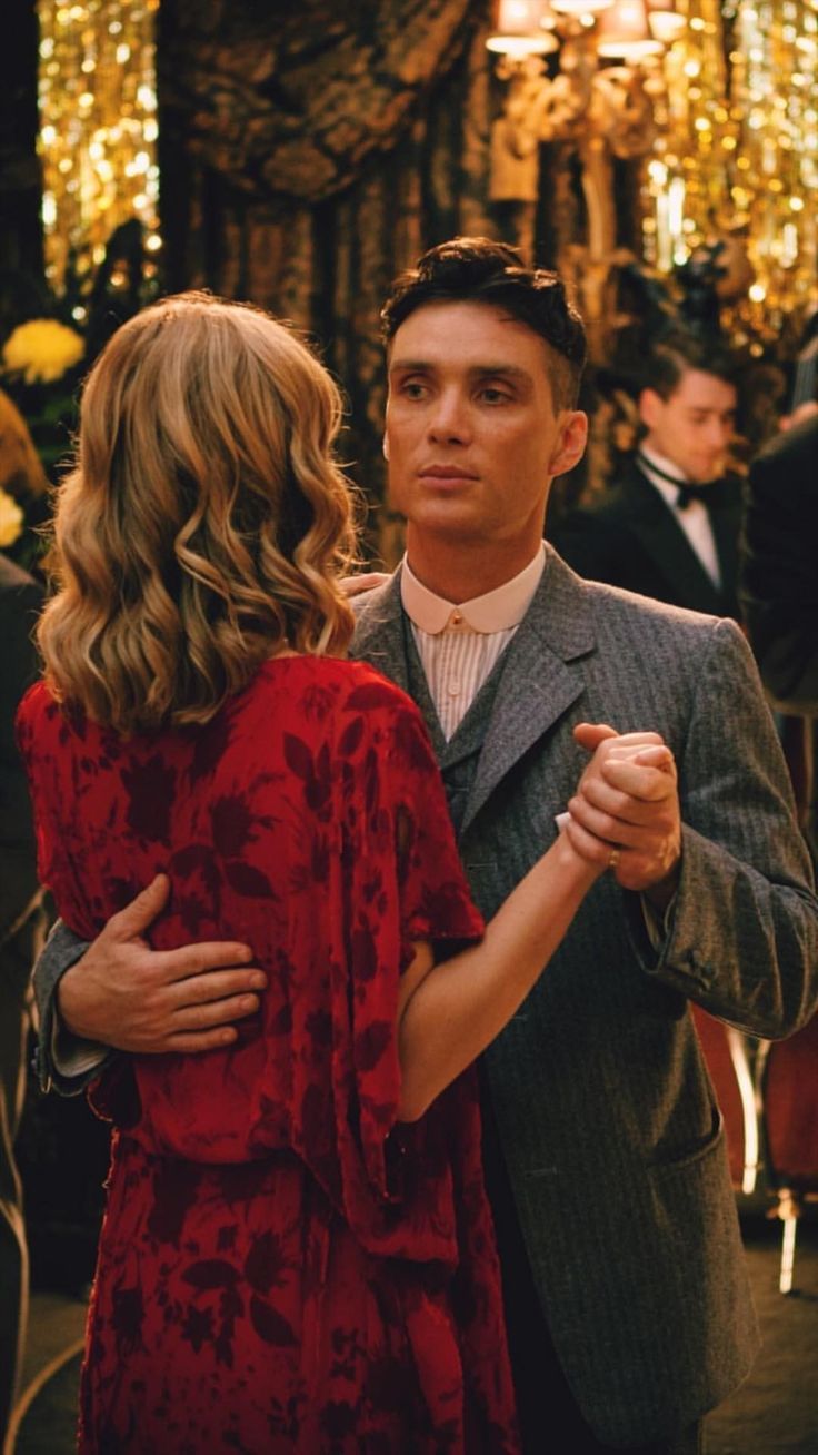 a man in a suit and tie dancing with a woman wearing a red floral dress